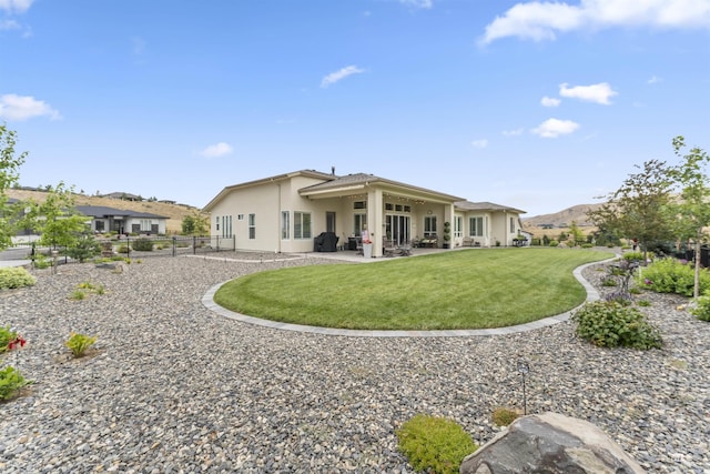 back of property with fence, a yard, a patio area, a mountain view, and stucco siding