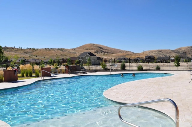 community pool featuring fence, a mountain view, and a patio