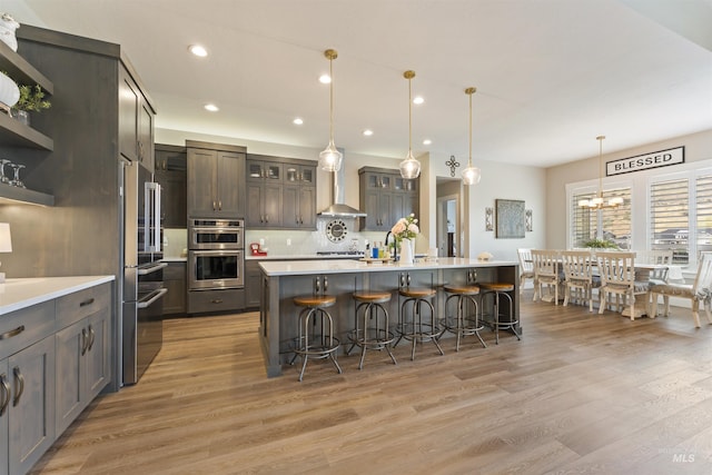 kitchen with decorative light fixtures, light countertops, glass insert cabinets, dark brown cabinets, and a large island with sink