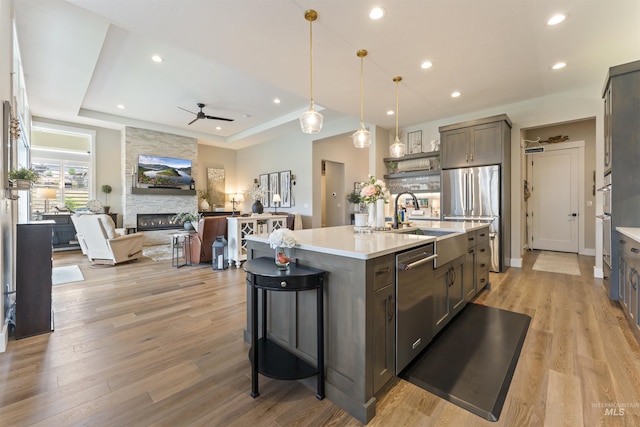 kitchen with open floor plan, a kitchen island with sink, a tray ceiling, stainless steel appliances, and light countertops