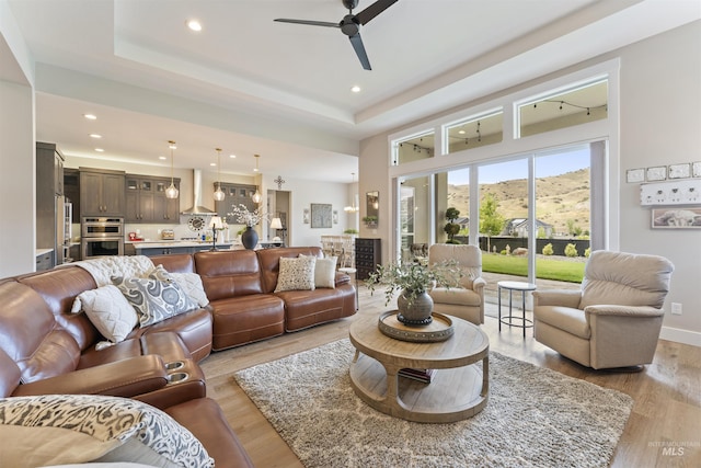 living room with a tray ceiling, light wood-type flooring, a ceiling fan, and recessed lighting