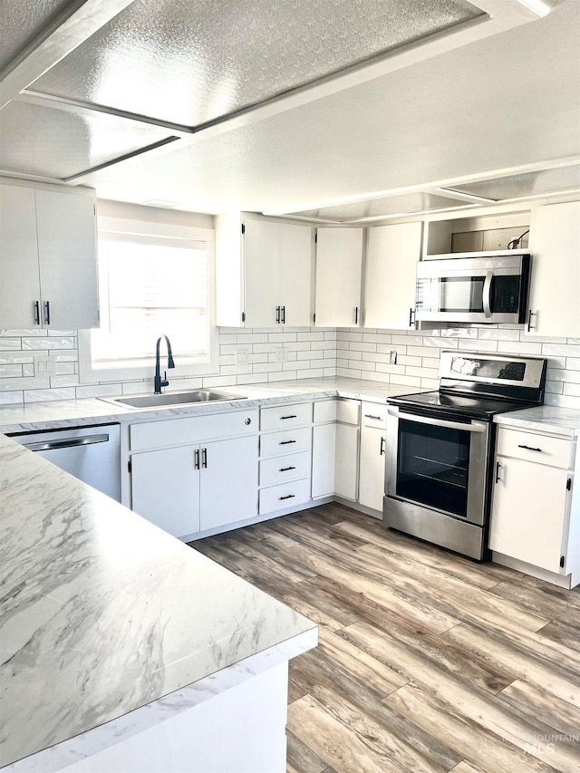 kitchen with tasteful backsplash, stainless steel appliances, sink, white cabinets, and light hardwood / wood-style flooring