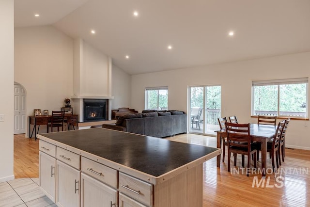 kitchen featuring high vaulted ceiling, a large fireplace, a kitchen island, dark countertops, and light wood finished floors