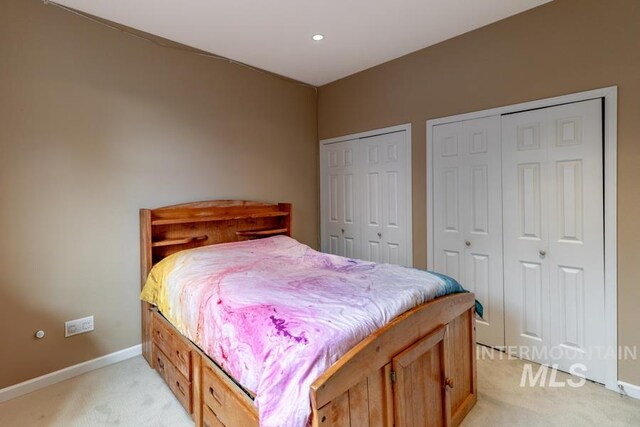 bedroom featuring light colored carpet, multiple closets, and baseboards