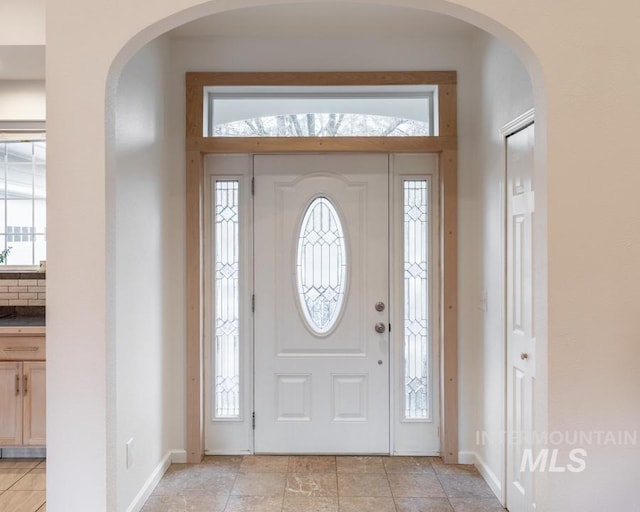 foyer entrance featuring arched walkways, baseboards, and a healthy amount of sunlight