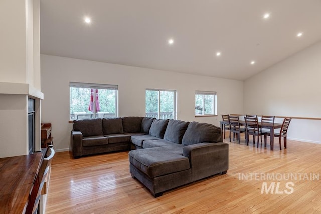 living room with light wood finished floors, vaulted ceiling, and a healthy amount of sunlight