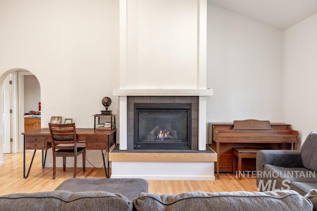 living area with high vaulted ceiling, arched walkways, a tiled fireplace, and wood finished floors