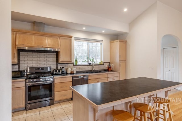 kitchen with under cabinet range hood, backsplash, a sink, light brown cabinets, and appliances with stainless steel finishes