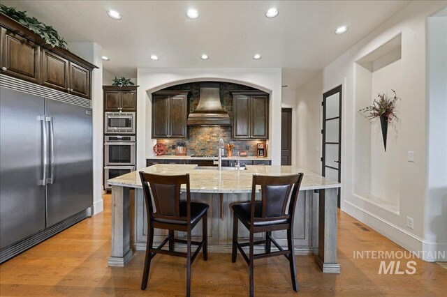 1480 N Colline Bello, Eagle, ID 83616 - kitchen featuring built in appliances, custom exhaust hood, backsplash, dark brown cabinets, and recessed lighting