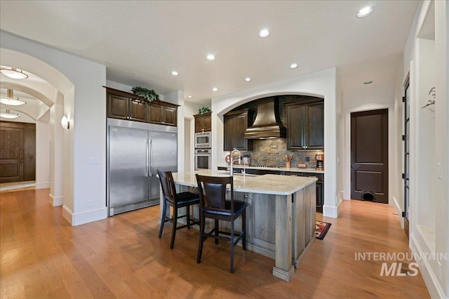 1480 N Colline Bello, Eagle, ID 83616 - kitchen featuring built in appliances, custom range hood, decorative backsplash, dark brown cabinetry, and arched walkways