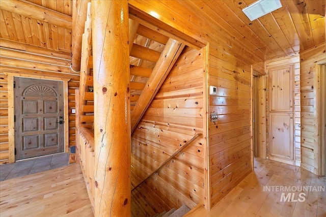 hall with light hardwood / wood-style flooring, wooden ceiling, and log walls