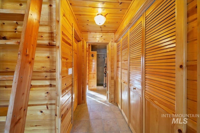 hallway with light tile patterned floors, wood ceiling, and wood walls