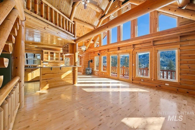 unfurnished living room with beam ceiling, light hardwood / wood-style flooring, high vaulted ceiling, wood ceiling, and a wood stove
