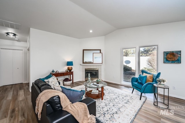 living room featuring hardwood / wood-style flooring, lofted ceiling, and a tile fireplace