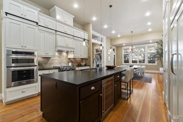 kitchen with pendant lighting, double oven, sink, wine cooler, and a kitchen island with sink