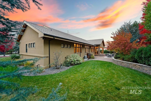 back house at dusk featuring a yard and a patio area