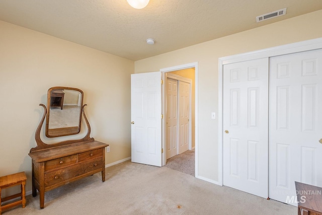 bedroom featuring a textured ceiling, light carpet, visible vents, baseboards, and a closet