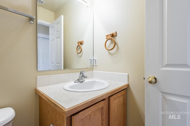 bathroom with visible vents, a textured wall, toilet, and vanity