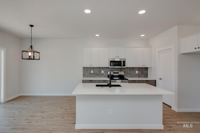 kitchen with pendant lighting, light countertops, appliances with stainless steel finishes, a sink, and an island with sink