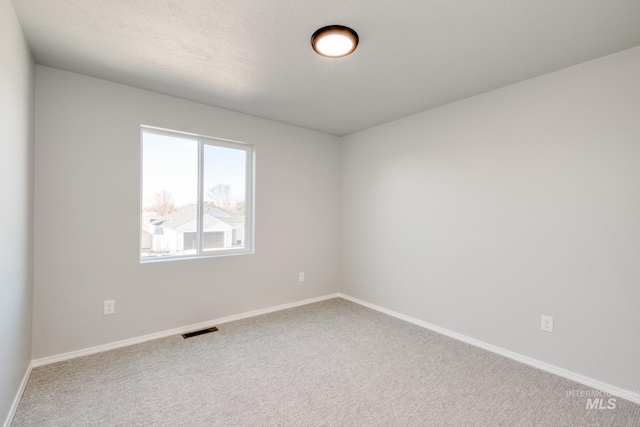 carpeted spare room with a textured ceiling, visible vents, and baseboards