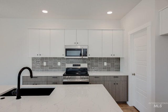 kitchen with light countertops, decorative backsplash, appliances with stainless steel finishes, white cabinets, and a sink