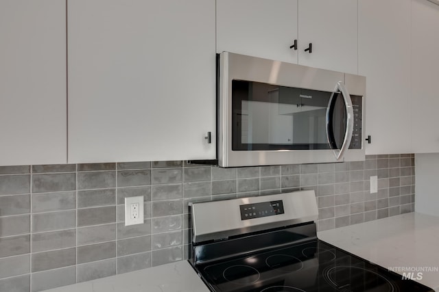 kitchen with appliances with stainless steel finishes, white cabinetry, backsplash, and light stone counters