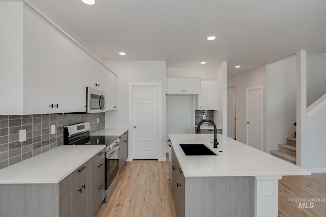 kitchen featuring appliances with stainless steel finishes, light wood-style floors, white cabinets, a sink, and an island with sink