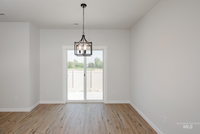 unfurnished dining area featuring light wood-type flooring, visible vents, baseboards, and an inviting chandelier