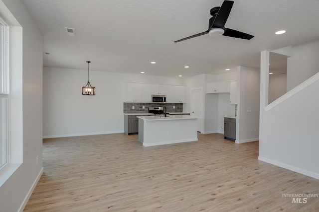 kitchen with hanging light fixtures, a kitchen island with sink, stainless steel appliances, light countertops, and white cabinetry