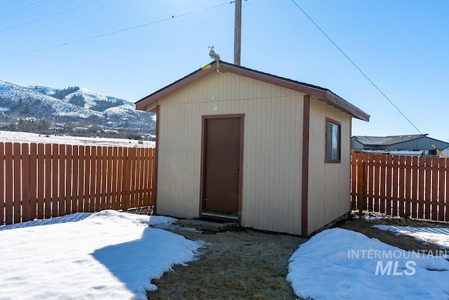 snow covered structure featuring a mountain view, an outdoor structure, a fenced backyard, and a storage shed