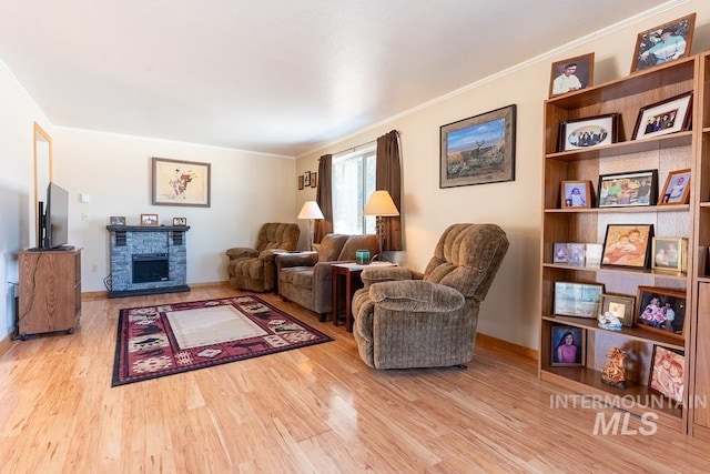 living area with a stone fireplace, wood finished floors, and ornamental molding