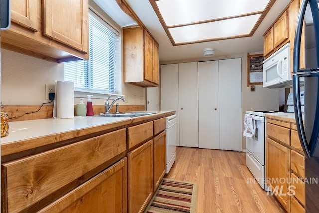 kitchen with white appliances, light countertops, light wood-type flooring, and a sink