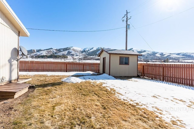 snowy yard featuring a mountain view, an outdoor structure, and a fenced backyard