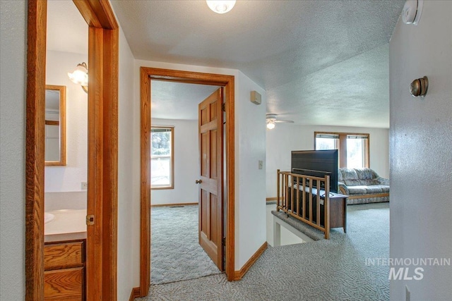 corridor with baseboards, a textured ceiling, an upstairs landing, and carpet flooring