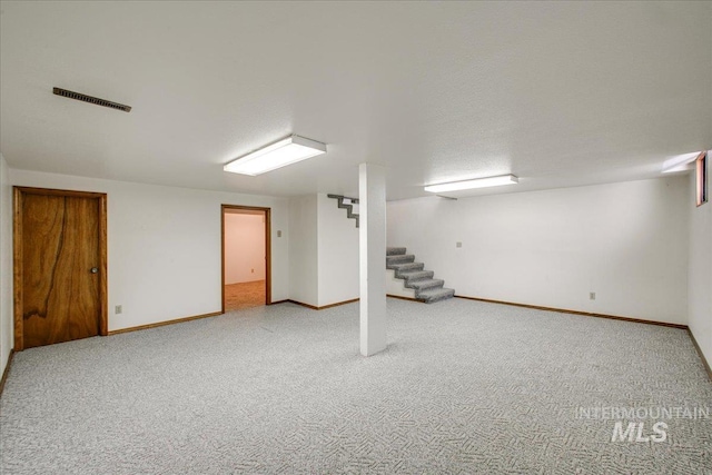 finished below grade area featuring stairway, baseboards, visible vents, and carpet floors