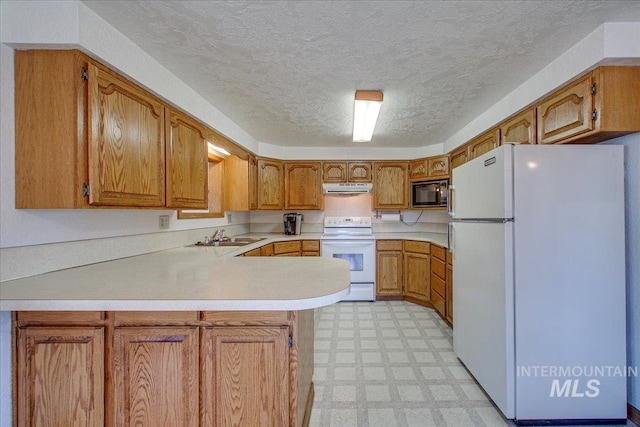 kitchen with under cabinet range hood, a sink, white appliances, a peninsula, and light floors