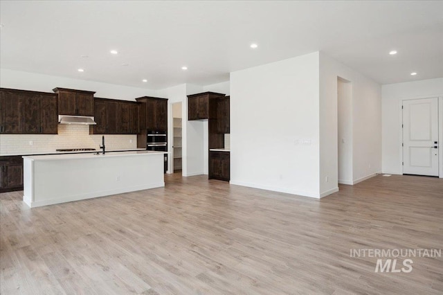 6139 W Burnt Sage Dr, Meridian, ID 83646 - kitchen featuring light wood-type flooring, recessed lighting, under cabinet range hood, a center island with sink, and backsplash