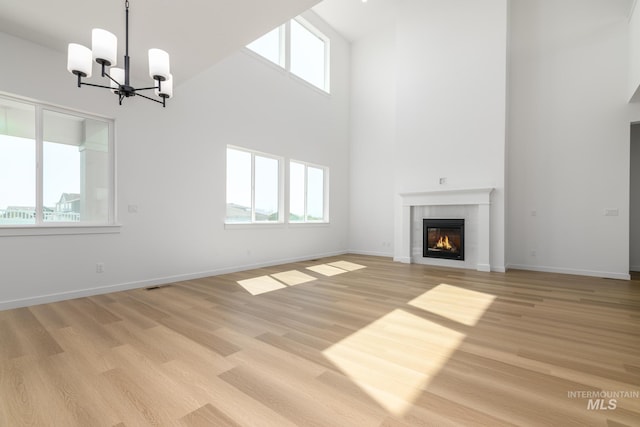 9124 W Patmore Ct, Star, ID 83669 - unfurnished living room with a towering ceiling, a chandelier, a tiled fireplace, light wood-style floors, and baseboards