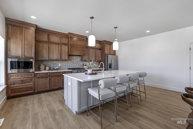 kitchen featuring a kitchen island with sink, baseboards, stainless steel appliances, and custom range hood