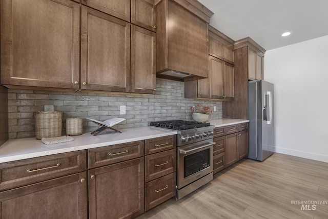 kitchen with light wood finished floors, tasteful backsplash, baseboards, premium appliances, and light countertops