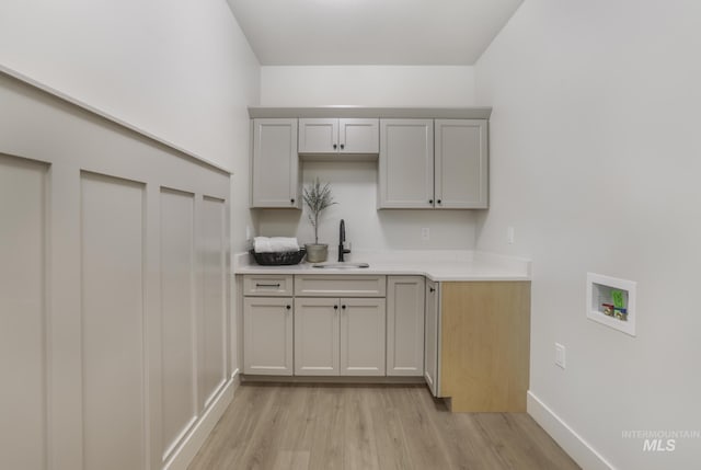 laundry area with a sink, cabinet space, light wood-style flooring, baseboards, and washer hookup
