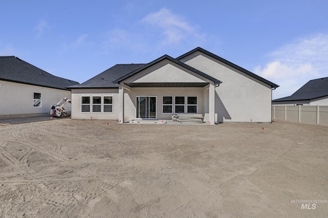 rear view of house with stucco siding and fence