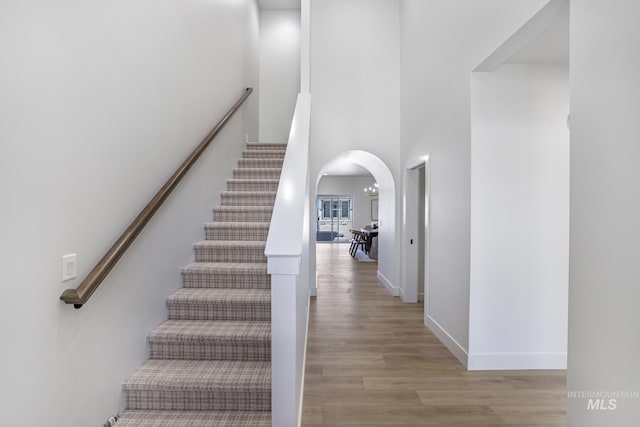 stairs featuring arched walkways, wood finished floors, a towering ceiling, and baseboards