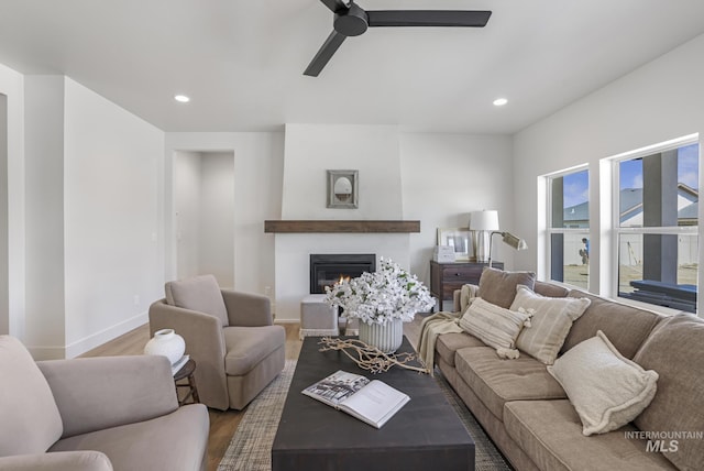 living area with ceiling fan, a glass covered fireplace, wood finished floors, and recessed lighting