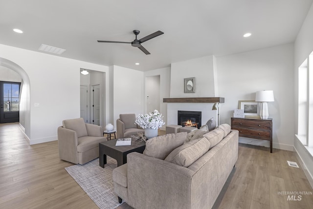 living room with light wood-type flooring, baseboards, a glass covered fireplace, and ceiling fan