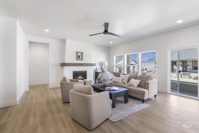 living area with a glass covered fireplace, light wood-type flooring, a healthy amount of sunlight, and a ceiling fan