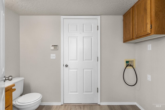laundry area featuring laundry area, baseboards, light wood-style floors, and a textured ceiling