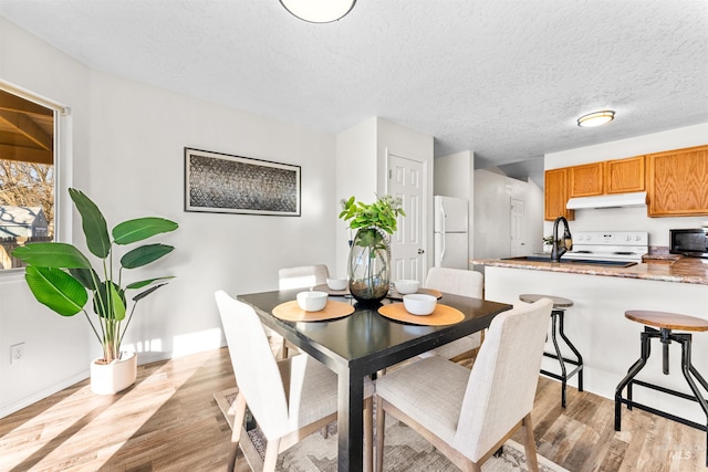 dining area featuring a textured ceiling, light wood finished floors, and baseboards