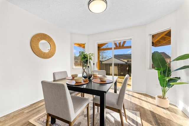 dining area with light wood-type flooring, a textured ceiling, and baseboards