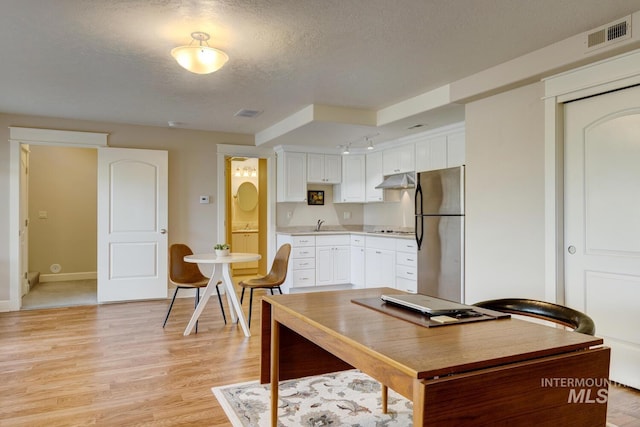 16089 N Basin Way, Boise, ID 83714 - kitchen with freestanding refrigerator, a textured ceiling, under cabinet range hood, white cabinets, and light wood-type flooring